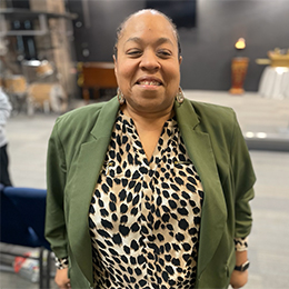 Sharonda Goode is seen smiling at the camera. She is wearing a green blazer over a leopard print blouse. Her hair is pulled back, and she is wearing earrings.