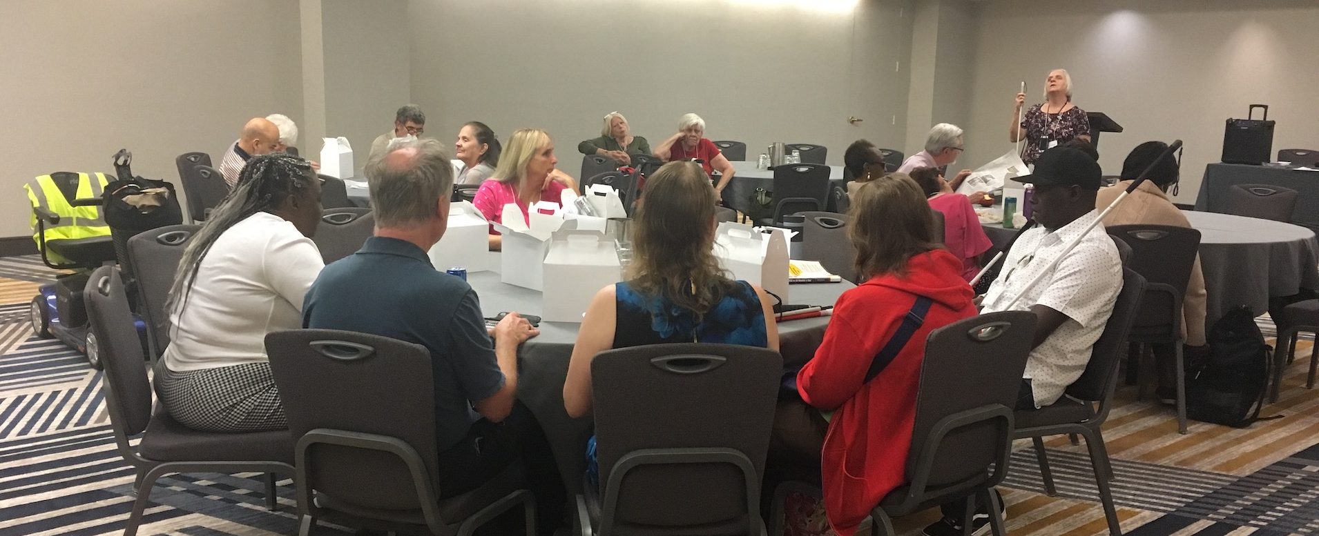 A large group of senior division members listening to Connie LeBlond speaking as she stands near their tables.